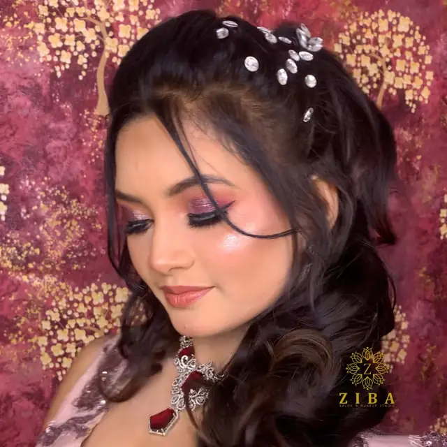 A close-up of a woman in soft pink eye makeup, loose curls pinned with pearl clips, against a deep pink textured backdrop.