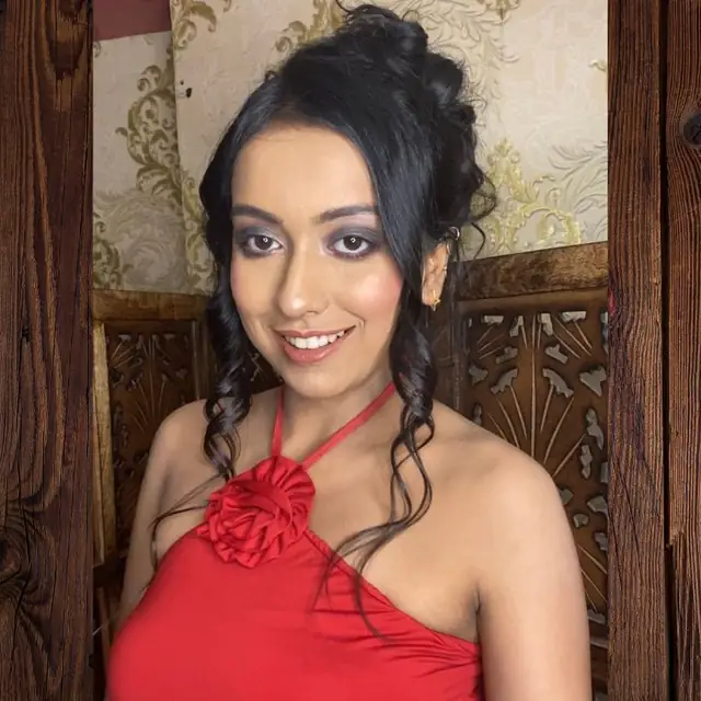 A woman in a red halter dress with a rosette at the shoulder and a soft updo, standing in front of a carved wooden door.